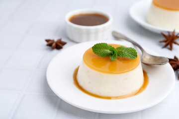 Tasty pudding with caramel sauce served on white tiled table, closeup. Space for text