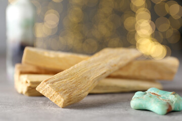 Palo santo sticks and gemstone on grey table against blurred lights, closeup