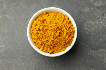Turmeric powder in bowl on grey table, top view