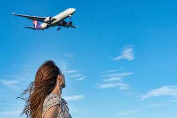 青空の下で飛行機を眺める女性
