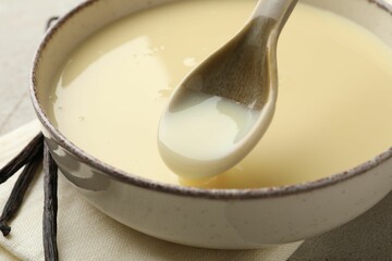 Taking tasty vanilla condensed milk with spoon from bowl on table, closeup