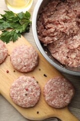 Many uncooked patties and spices on wooden table, flat lay