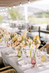 Bouquets of flowers in vases stand on the festive table among glasses and plates