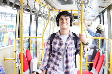 Positive Gen Z Asian Male In Casual Style With Headphone Standing While Holding Pole In The Bus