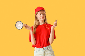 Young pretty female lifeguard in cap with whistle and megaphone on yellow background