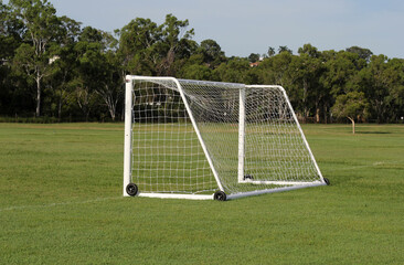 Portable soccer football goal sitting on a grassy field with trees in the background