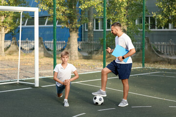 Young man training teenage boy to play soccer outdoors