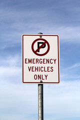No Parking - Emergency Vehicles Only road sign with a sky with scattered clouds background