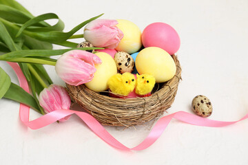 Nest with Easter eggs, chicks and beautiful tulip flowers on white background