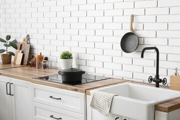 Kitchen counters with stove, utensils and sink near white brick wall
