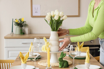 Woman with tulips on dining table set for Easter in kitchen