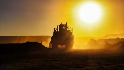 silhouette of truck mining equipment and front loader at a diamond mine ,outdoors sunset with orange sky and sun reflection rays late in the day © poco_bw