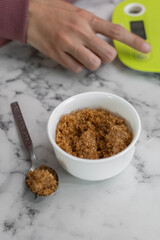 A hand carefully calibrating the scale to ensure accuracy before weighing rich brown sugar, highlighting the attention to detail in preparing ingredients for a recipe.

