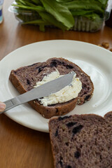 A close-up of a knife spreading creamy cheese on a fresh slice of bread, creating a delicious and smooth base for a simple yet satisfying snack.

