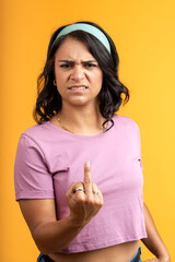 Woman showing middle finger with angry expression on yellow background