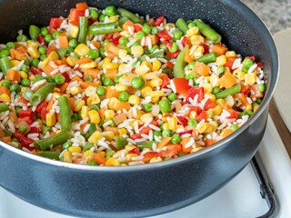Close-up of colorful mixed vegetables with rice in a black pan on a stove