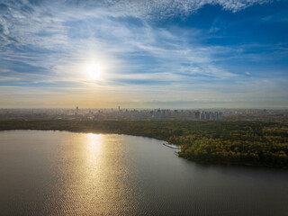 Autumn forest on lake shore at sunset and city on horizon, auerial view