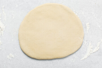 Overhead view of doughnut dough being rolled on a white countertop, top view of doughnut dough on a white countertop, process of making doughnut