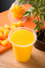 Mango smoothie in plastic cup on orange tablecloth
