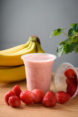 Strawberry and banana smoothie in plastic glass on wooden table
