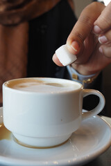 Hand adding sugar to a warm cup of coffee in a cozy cafe setting