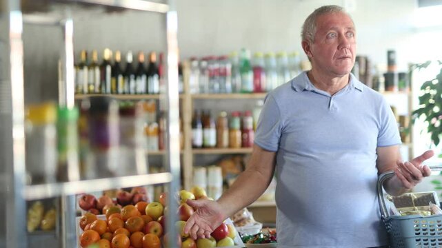 Elderly man buyer with basket of food forgot what he wanted to buy at grocery store
