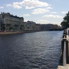 Obraz premium View of Neva River embankment in Saint Petersburg with historic buildings under a partly cloudy sky. Captured in daylight displaying reflections in the water and architecture along the canal. 
