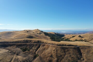 Aerial drone view of golden rolling hills and shinny roads under clear Sky in California.