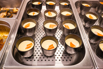Metal cups filled with creamy pudding garnished with orange slices arranged in rows on a stainless steel tray