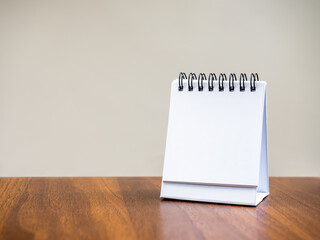 Blank page of desk spiral calendar for organizer concept to plan and reminder, standing on wooden table and grey background. Mock up small table calendar paper, front view, template photo for design.
