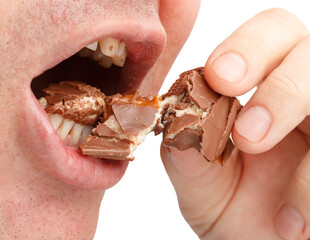 A man is eating a chocolate bar with his teeth showing