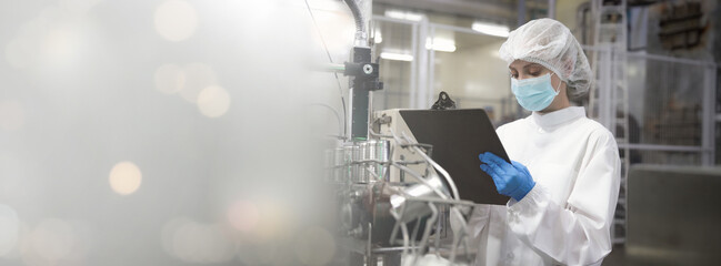 A woman in a white lab coat and blue gloves is looking at a clipboard. She is wearing a face mask.