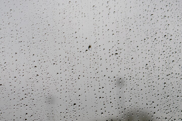 Raindrops on window glass against the moody grey British sky create a natural pattern. Water droplets on a transparent surface capture the minimalist texture during typical overcast weather