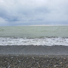 Serene seascape featuring gentle waves lapping against a pebbly beach under a cloudy sky. The calm waters and muted colors evoke tranquility and natural beauty. Ideal for outdoor and relaxation themes