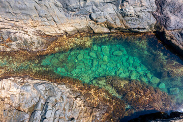 Aerial view of hidden emerald pool in volcanic rocks at Aguas Verdes, Fuerteventura. Ocean waves crash against rugged coastline revealing stunning natural tidal pool
