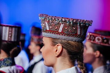 Fototapeta premium A close-up of a woman wearing an ornate beaded traditional Baltic headdress during a cultural performance, surrounded by others in similar folk attire