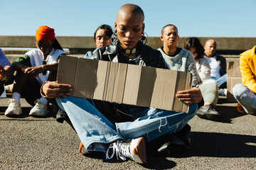 Young woman sitting on highway during a peaceful protest holding cardboard sign