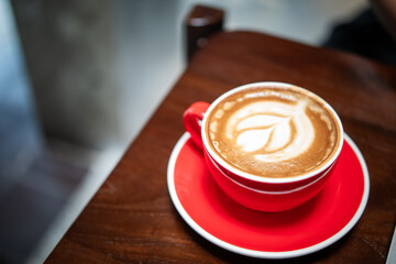 Top view of latte art in a red ceramic cup on matching saucer, placed on wooden café table with blurred modern background, showcasing warm coffee culture and cozy atmosphere in an Asian coffee shop