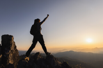 Silhouette of  A person standing on top of the mountain with their arms raised in victory, overlooking misty mountains and clouds at sunrise.  Success and goal achievement. People success