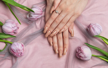 Woman showing nude manicure with engagement ring near pink tulips