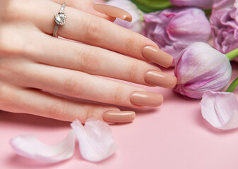 Woman showing stylish nude manicure near purple tulips on pink background