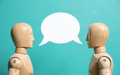 Obraz premium Two wooden figures face each other against a teal background. A blank white speech bubble floats between them, suggesting conversation and exchange of ideas.