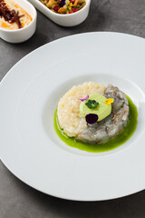 Gourmet shrimp and white fish tartare with avocado mousse, edible flowers, and green sauce, served on a white plate