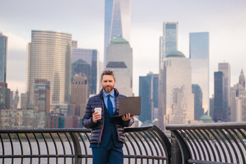 Handsome business man in suit near NYC. Outdoor business. Serious businessman standing against skyscraper in New York, at Manhattan. Professional employee waiting for business partners outdoors.