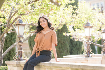 Young woman sits on a stone ledge, smiling amidst lush greenery