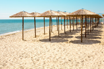 Row of wooden umbrellas at sandy beach, sea and blue sky