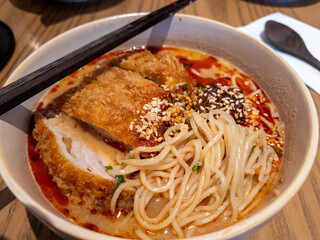 Close up of a bowl of hot chilli spicy hand pulled noodles soup served with fried port chop in a crispy coating.