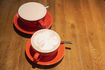 Two red cups of coffee on wooden table showcasing intricate latte art.