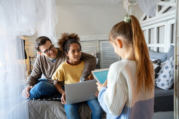 Excited single father plays with diverse, multi-ethnic daughters. Using digital tablet enjoy weekend
