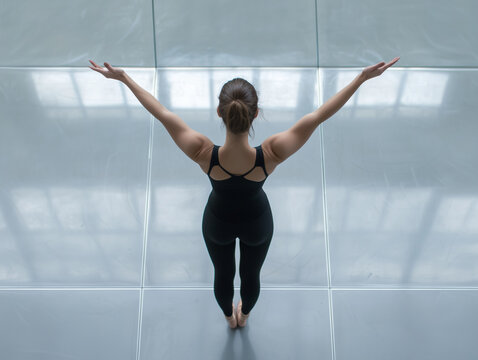 Aerial view of female dancer practicing ballet gracefully in studio, arms elegantly raised, reflecting tranquility and dedication in minimalist setting